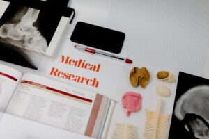 Medical research materials including anatomical models, X-rays, a textbook, and a smartphone laid out on a white surface